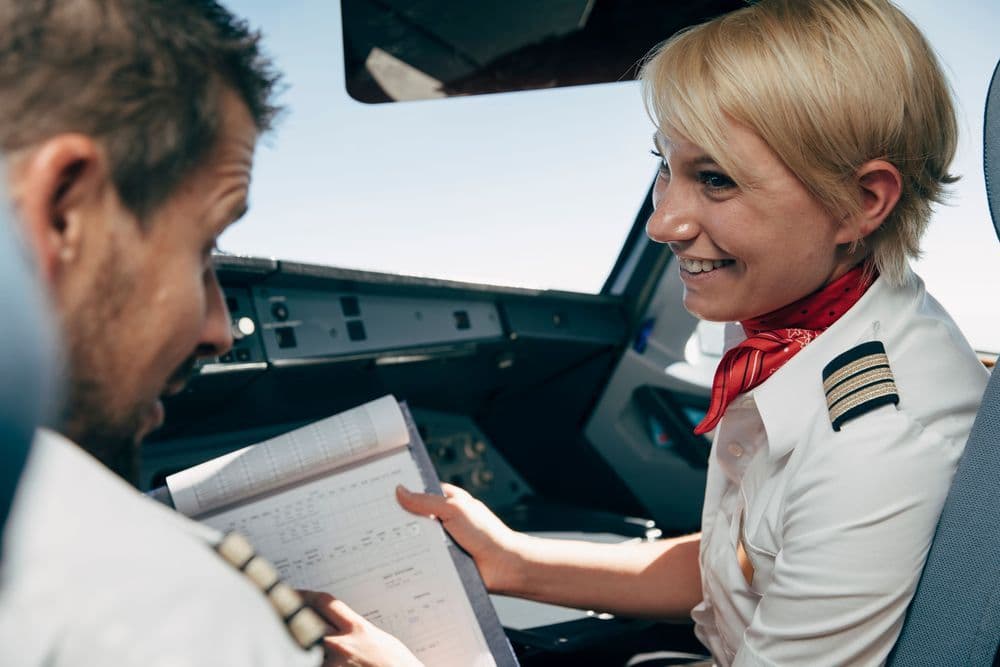 Eine Airlinepilotin sitzt im Cockpit und spricht mit dem anderen Piloten