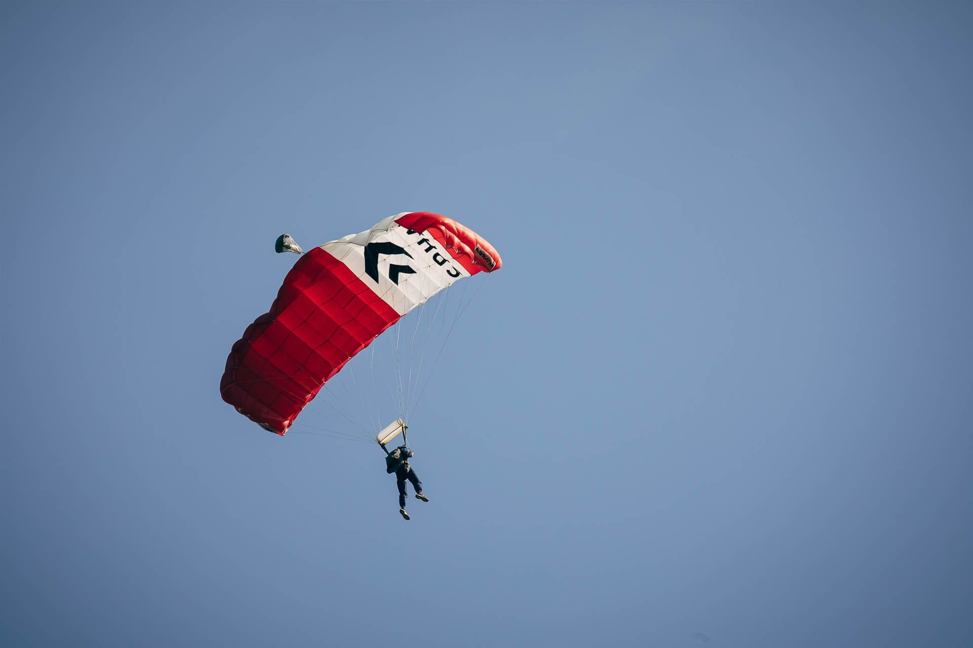 Ein Fallschirmspringer mit geöffnetem Schirm fliegt bei blauem Himmel der Landung entgegen