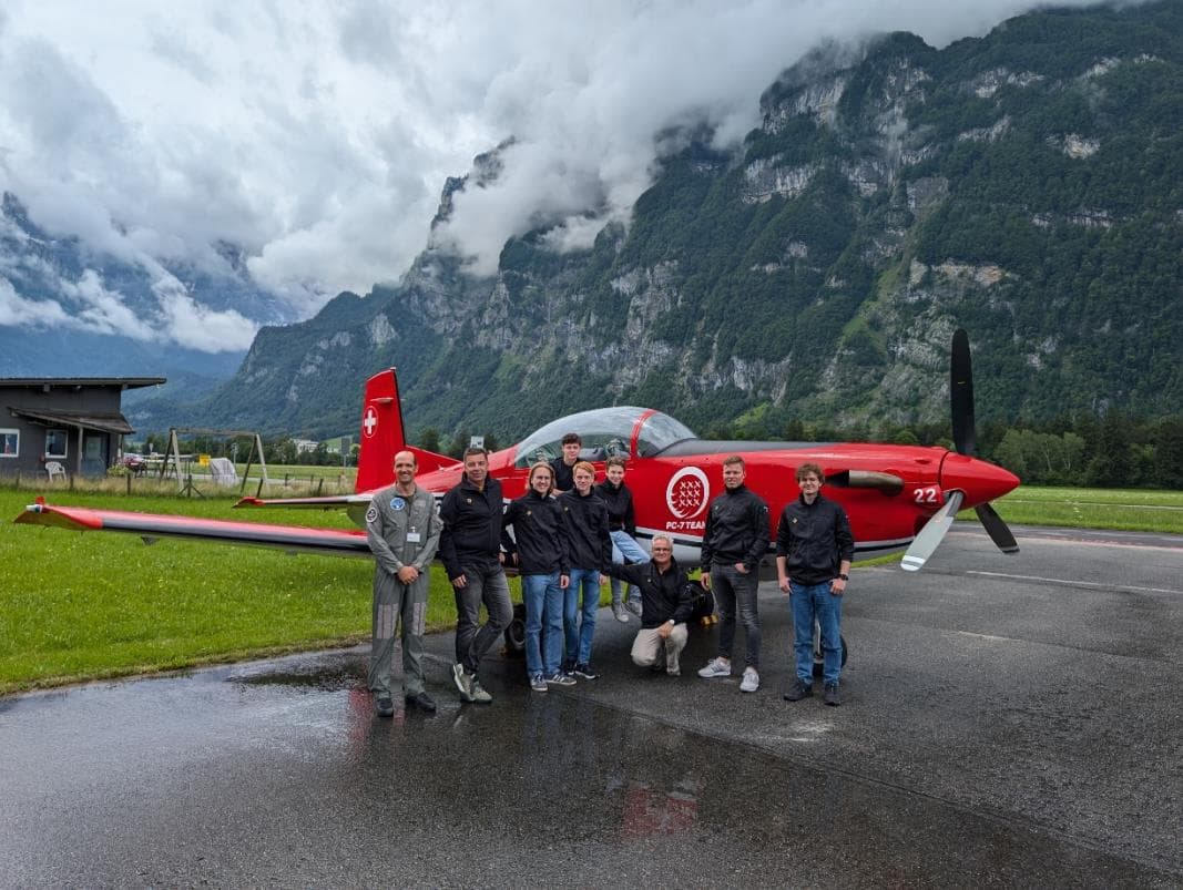 Teilnehmende und Fluglehrer stehen vor einem parkierten PC-7 auf einem Flugfeld